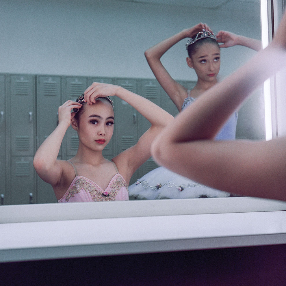two young ballerinas fix their hair pins in front of the mirror in costume.