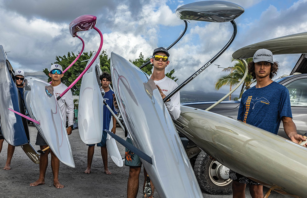 group of five young men holding small boats by the beach.