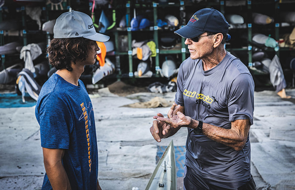 two men in athletic shirts and caps talking to each other.