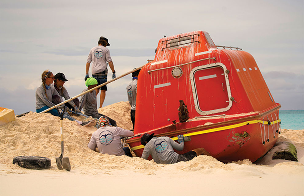 bright orange vessel on the sand of the beaches with three environmentalists in the background.