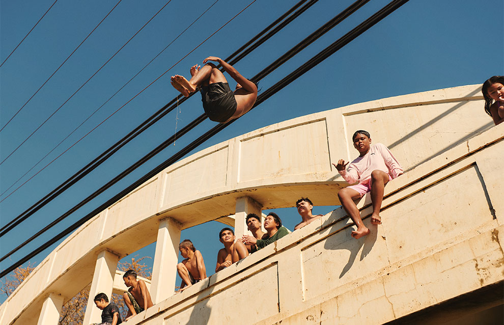 boys hanging out on a sunny day on the bridge while one boy cannonball jumps off.