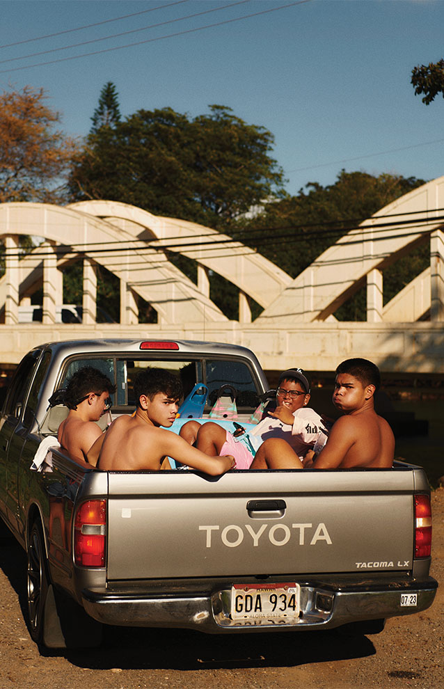 young men in back of grey pick-up truck with bridge in the background.