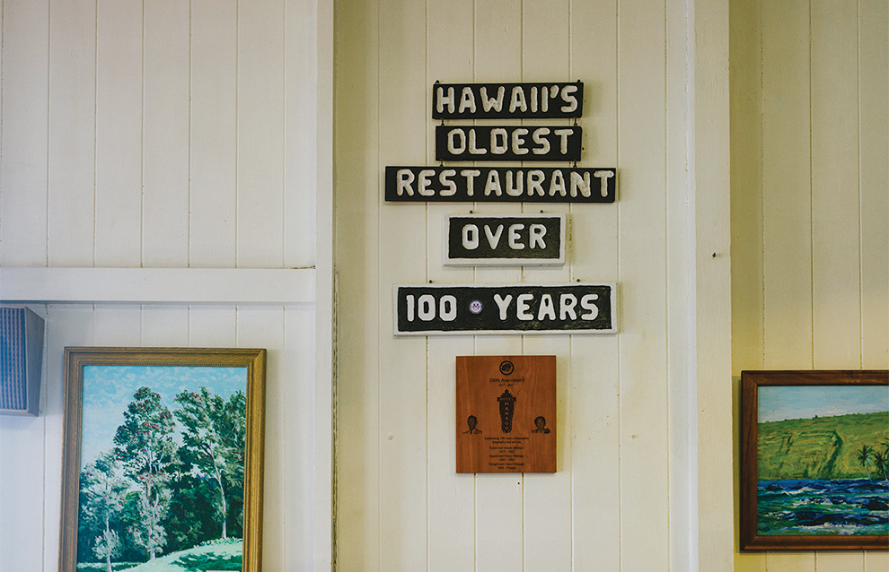 A wall with portraits and a restaurant sign that show when it was established.